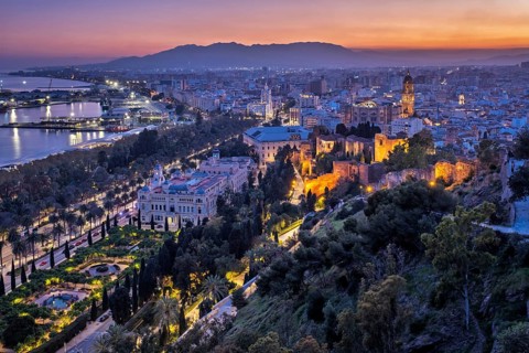 Wide twilight panorama of Malaga, Spain, with illuminated Cathedral and Alcazaba walls above the