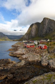 Traditional red Rorbuer huts on rocky coast in the fishing village of Hamnøy against steep mountain
