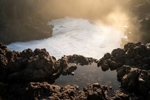 Seawater collects in a small pool, spray rises in the backlight. In the morning. La Fajana, La