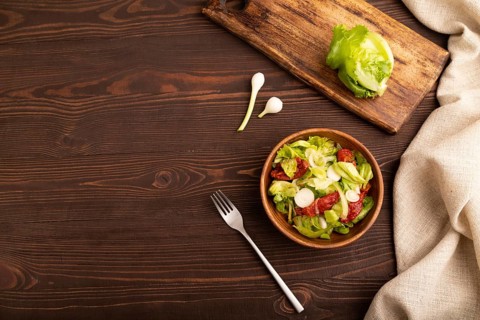 Mixed salad with lettuce, tomatoes, onion and vegetables in wooden bowl on brown wooden background