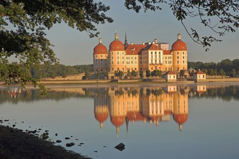 Baroque castle with reflection in lake and shore, yellow baroque castle with corner towers,