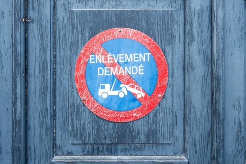 Round, red-blue parking sign with the inscription ENLÈVEMENT DEMANDÉ and a tow truck symbol on a