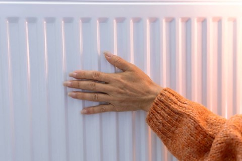 Close-up of a hand adjusting the temperature on a radiator thermostat, regulating home heating for