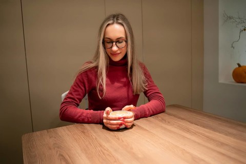 Young woman in red and burgundy sweater with coffee at wooden table, A woman wearing glasses and a