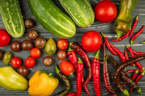 Fresh, colorful vegetables such as cucumbers, tomatoes, peppers, hot peppers on dark wood