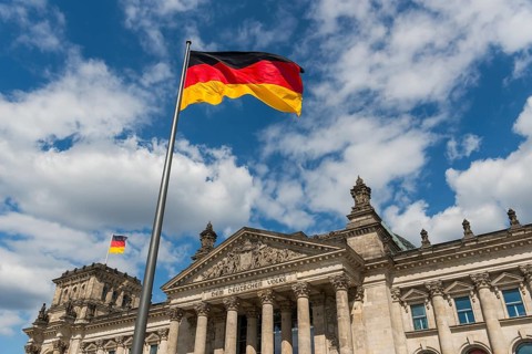 German flags are blowing in the wind in front of the German Reichstag in sunshine and blue sky,