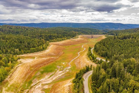 View of an empty riverbed surrounded by forest and a winding road, rehabilitation of the