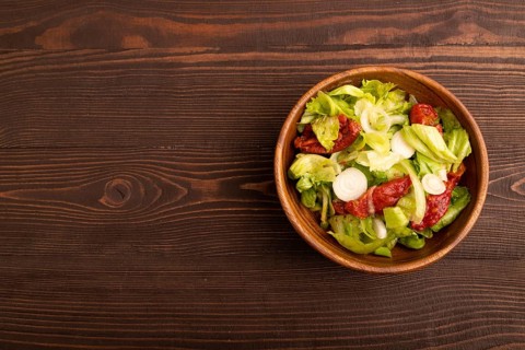 Mixed salad with lettuce, tomatoes, onion and vegetables in wooden bowl on brown wooden background.