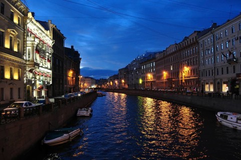 An atmospheric night scene with illuminated buildings that are reflected in the water of a river,