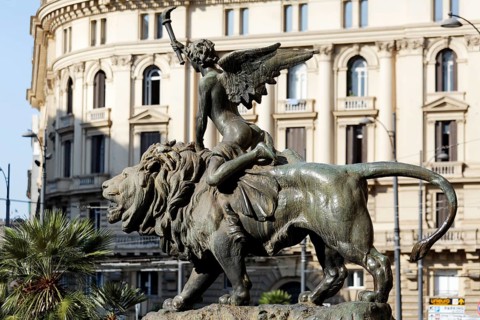 Winged boy riding on a lion, allegorical bronze sculpture in front of the Palazzo della Borsa,
