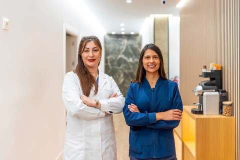 Two confident female practitioners one in a lab coat, one in blue scrubs stand with arms crossed in