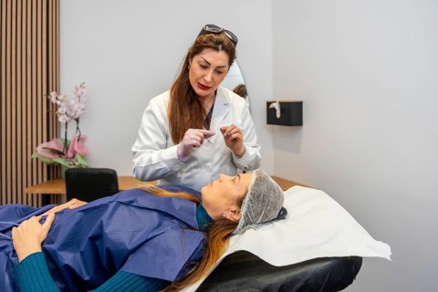 Doctor engaging with a lying patient wearing a hair net and a protective gown, discussing a beauty