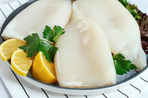 Fresh squid on a black plate with greens and lemon slices prepared for cooking in a kitchen setting