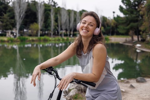 Young Caucasian woman with brown hair and pink headphones smiles while leaning on an electric