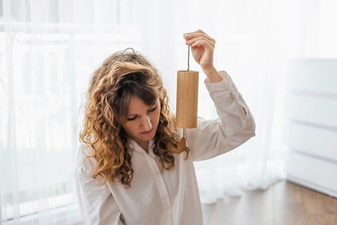 A woman with curly hair holding a wooden chime in a softly lit room