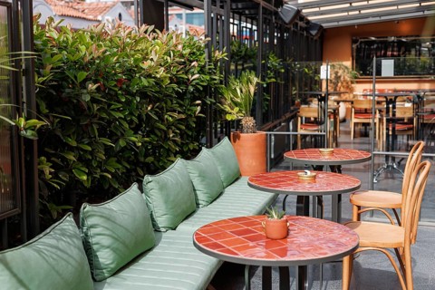 European restaurant or cafe. Outdoor seating with green cushions and red tiles, surrounded by