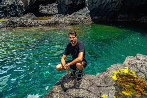 Man crouching on volcanic rock, enjoying a relaxed vacation day by the clear turquoise natural