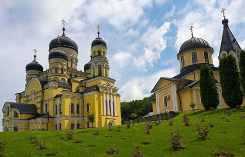 Orthodox church on green hill with yellow and black domes under blue sky, Hîncu monastery, Hâncu,