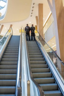 Two people stand at the top of an escalator in a modern shopping center, Milaneo, Stuttgart,