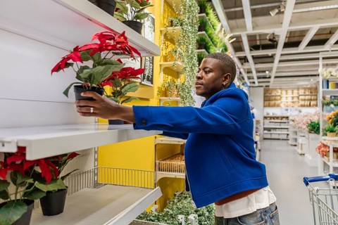 A person stands in a home goods store during the afternoon and arranges a red flower pot on a shelf