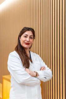 Female doctor in white coat smiling with arms crossed against a modern wooden slatted wall in an