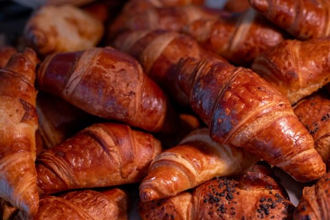 A variety of golden-brown croissants featuring crispy layers and sprinkled with sesame seeds are