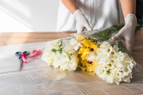 A florist with white gloves arranges vibrant white and yellow flowers, carefully wrapping them in