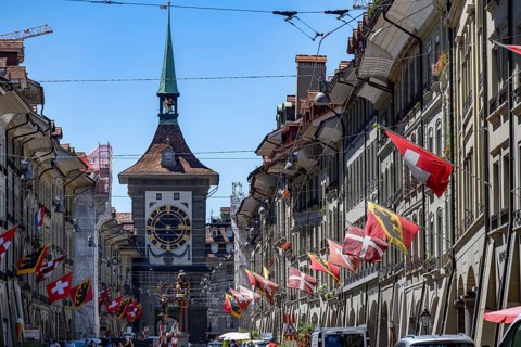 Kramgasse with historic houses decorated with cantonal flags and Swiss national flags, back clock