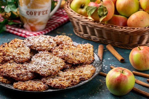 Apple cookies sprinkled with powdered sugar, coffee cup and apples behind