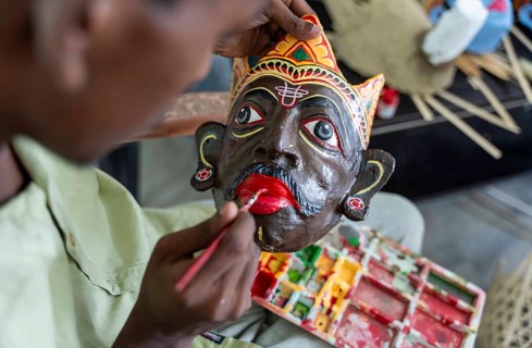 A student paints the facial details of a traditional mask at a mask-making workshop during an