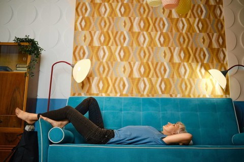 Dreamy woman relaxes on couch in cozy living room with stylish wall design and soft lighting. This