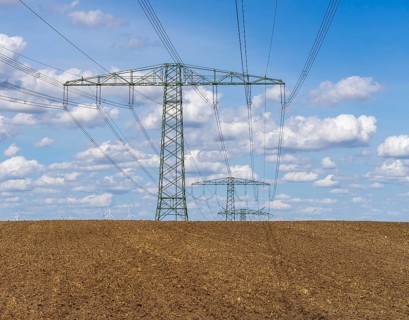 Wide agricultural landscape with freshly plowed fields and high-voltage lines as well as wind