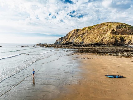 Woman and dog with kayak on Beach from a drone, North Devon and Cornwall Coastpath Border from a