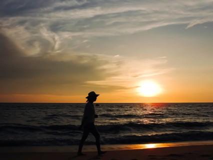 A woman walking along the beach during sunset, silhouetted against the orange sky and ocean