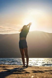 Backlit by the low sun, a woman practices an Urdhva Hastasana yoga variation, Upward Salute, with