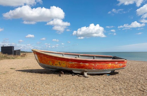 Coastal landscape of old red boat on beach with blue sky cumulus cloud, Dunwich, Suffolk, England,