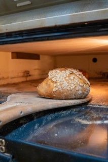 A golden brown bread with oats is taken out of the oven with a wooden shovel, bake bread,