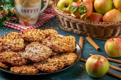 Apple cookies are sprinkled with powdered sugar, coffee cup and apples behind