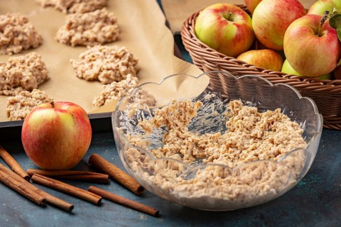Raw cookies on a baking sheet next to apples and dough bowl