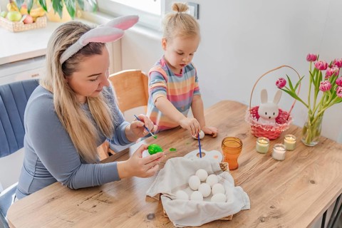 Mother and toddler girl daughter painting Easter eggs at home in modern kitchen. family tradition,