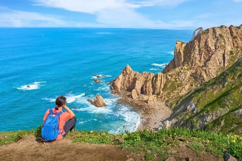 Woman hiking on the coastline of Cabo Raso Lighthouse, Atlantic West coast, Portugal