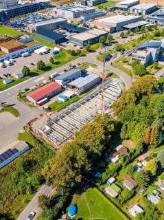 Aerial view showing a construction site in an urban area with industrial buildings and vegetation,