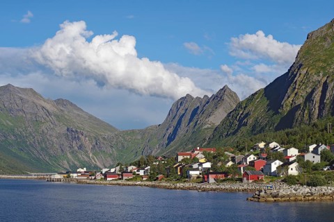Small picturesque settlement on a fjord surrounded by imposing mountains under a clear blue sky,
