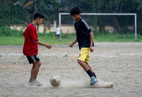 Children play football on a dusty neighbourhood field, chasing the ball with energy and
