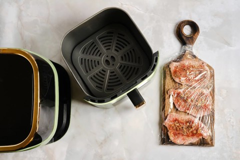 Raw pork meat seasoned with spices on cutting board next to air fryer. Air fryer is preheated and