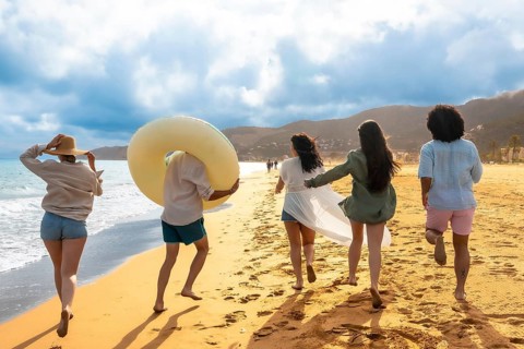 Diverse group of young women friends happily running barefoot into the ocean water on a sandy beach