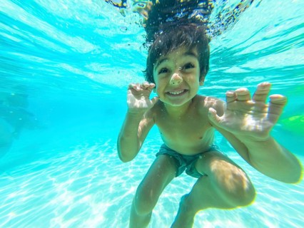 Young child playing and smiling underwater, enjoying a refreshing dip in the clear blue swimming