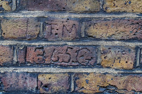 Secret London. Carved initials sit above a scratched collar number on adjoining bricks along