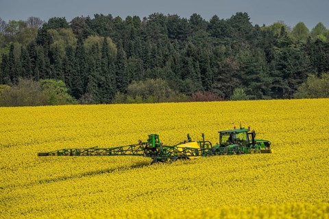 Agriculture, rapeseed field in full bloom, farmer sprays the field with a John Deere M952 trailer