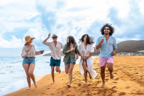 Young diverse people running barefoot on the sandy beach shoreline, laughing and celebrating their
